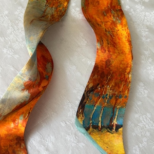 May include: A long, narrow scarf featuring an abstract landscape print with vibrant shades of orange, yellow, and deep blue. The design depicts stylized trees and foliage in a painterly style, with a smooth, flowing texture and finished edges.