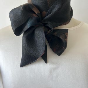 May include: A black silk scarf with a floral print. The scarf is tied around a mannequin's neck in a bow.
