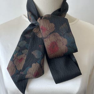 May include: A black silk scarf with a floral print featuring brown, pink, and blue flowers. The scarf is tied in a bow around a white mannequin's neck.