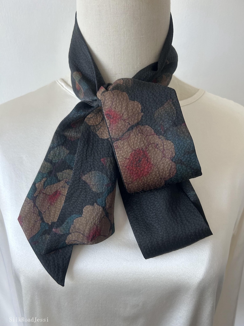 May include: A black silk scarf with a floral print featuring brown, pink, and blue flowers. The scarf is tied in a bow around a white mannequin's neck.