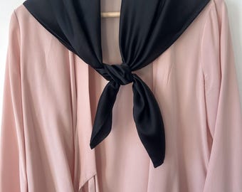 Könnte beinhalten: Eine rosa Bluse mit einem schwarzen Satin-Schal, der um den Hals gebunden ist.