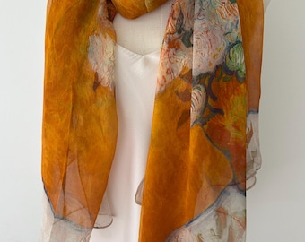 Puede incluir: Una bufanda ligera que presenta un color base amarillo mostaza vibrante con un intrincado estampado floral en tonos blancos, verdes y naranjas suaves. La tela tiene una textura delicada y semitransparente con un dobladillo acabado en los bordes.