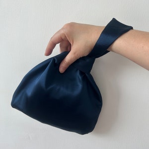 May include: A dark blue satin clutch bag with a knotted handle.