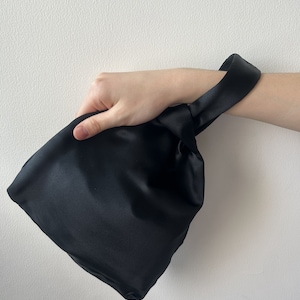 May include: A black satin clutch bag with a knotted handle.