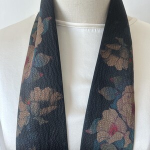 May include: A black silk scarf with a floral pattern in shades of brown, pink, and blue. The scarf is folded in half and draped over a white mannequin.