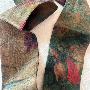 May include: A brown, green, and red patterned ribbon with a textured surface. The ribbon is folded in half and the pattern is visible on both sides.