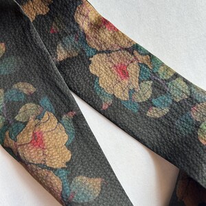 May include: A black fabric ribbon with a floral print. The flowers are a muted brown, pink, and blue. The ribbon is textured and has a subtle sheen.