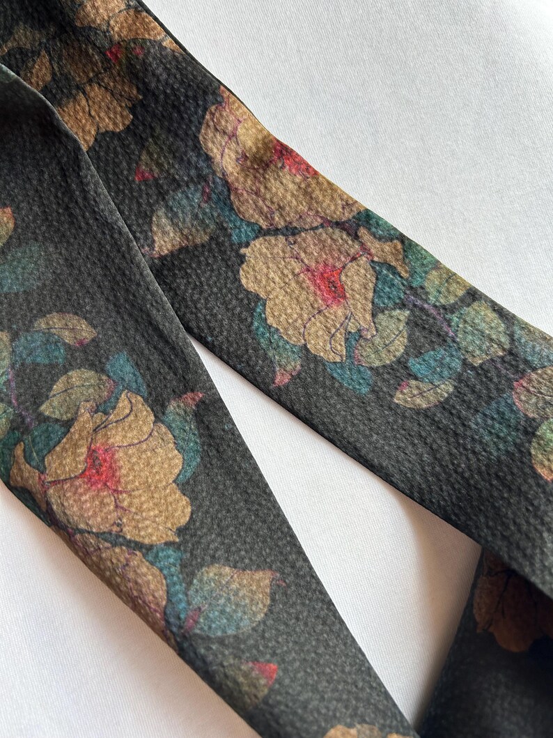 May include: A black fabric ribbon with a floral print. The flowers are a muted brown, pink, and blue. The ribbon is textured and has a subtle sheen.
