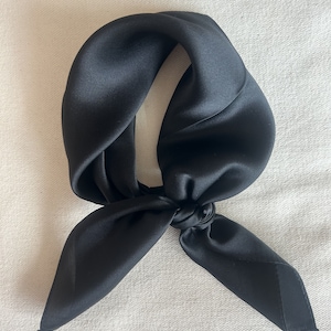 May include: A black silk scarf tied in a knot. The scarf is folded in half and the ends are tied together.