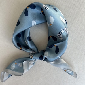 May include: A light blue silk scarf with a white and black floral pattern. The scarf is tied in a knot and has a white border.