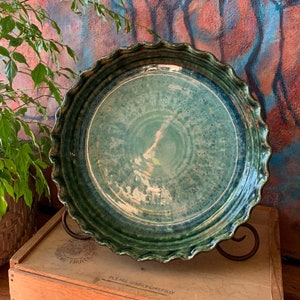 May include: A green ceramic pie plate with a scalloped edge. The plate has a white glaze with a green and blue swirl pattern. The plate is sitting on a wooden box with the text "Please handle carefully" printed on it.