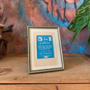 May include: A framed card with a blue background and white text that reads "5 in 1 by Metalcraft with ready made mats to fit your snapshots in all these sizes... 2x2, 3x3, 3 1/2 x 5, 4x6, and 4x5 without mat. Easy Instructions." The card is in a silver frame with a white mat.