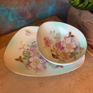 May include: A set of two white porcelain serving dishes with a floral design. The larger dish is a shallow oval shape and the smaller dish is a round bowl. Both dishes have a light green glaze and are decorated with pink and white roses.