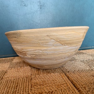 May include: A large, white and beige ceramic bowl with a textured, wavy design. The bowl is sitting on a woven rug.