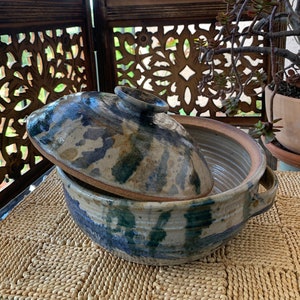May include: A blue and brown ceramic casserole dish with a lid. The dish has a rustic, handmade look and is decorated with a blue and green glaze.