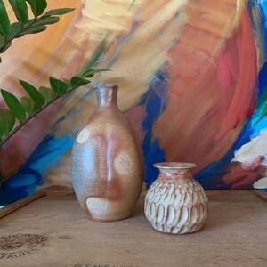 May include: Two ceramic vases, one tall and slender with a brown, white, and gray glaze, and the other shorter and rounder with a white glaze and a textured surface.