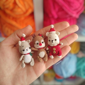 Può includere: Tre piccoli ornamenti natalizi all'uncinetto: un cane, una renna e un orso. Ogni figura indossa un cappello e un abito festivo, con l'orso in un completo rosso. Gli ornamenti sono fatti a mano con cuciture dettagliate.