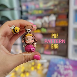 Könnte beinhalten: Handgefertigte Häkelpuppe mit rosa Kleid, die einen Ballon mit einer gehäkelten Biene hält. Ein kleiner Teddybär sitzt auf dem Kopf der Puppe. Der Text "PDF PATTERN ENG" ist im Bild zu sehen.