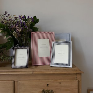 May include: Three striped picture frames on a wooden dresser. The frames are red and white, blue and white, and black and white. The frames are all the same size and shape.