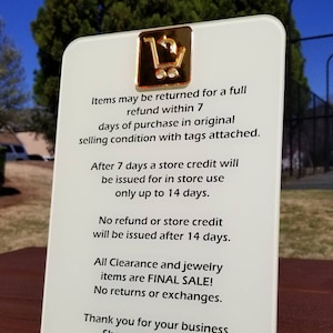 May include: White sign with a gold shopping cart icon and text that reads: "Items may be returned for a full refund within 7 days of purchase in original selling condition with tags attached. After 7 days a store credit will be issued for in store use only up to 14 days. No refund or store credit will be issued after 14 days. All Clearance and jewellery items are FINAL SALE! No returns or exchanges. Thank you for your business. Shop with us online @4allherkind.com"