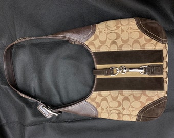May include: A brown and beige Coach shoulder bag with a suede trim and a silver metal clasp. The bag features the signature Coach pattern.