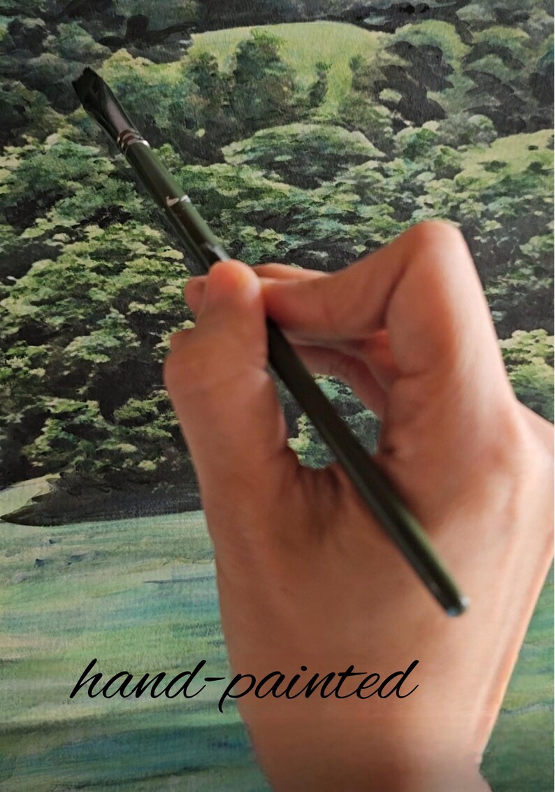 Op de afbeelding: Een hand houdt een zwart penseel boven een groen-blauw aquarel schilderij. Het schilderij toont een landschap met bomen en gras. De tekst "hand-painted" is in zwart onder de kwast geschreven.