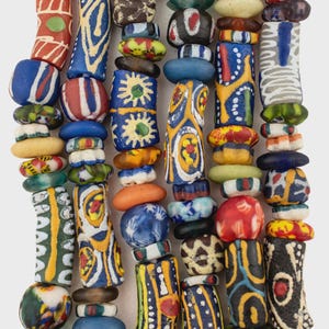 May include: A collection of multi-colored glass trade beads arranged in vertical strands. The beads feature diverse shapes, including cylindrical, spherical, and flattened forms, decorated with intricate patterns in red, blue, yellow, green, and white.