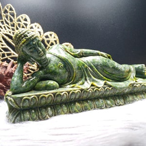 Puede incluir: Estatua de Buda reclinado de jade verde, con una expresión serena, descansando sobre una base de loto. La estatua está tallada con intrincados detalles y tiene una presencia tranquilizadora.