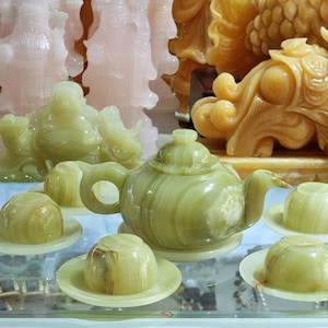 May include: A green jade tea set with a teapot, cups, and saucers. The set is made of polished jade and has a natural, earthy look.