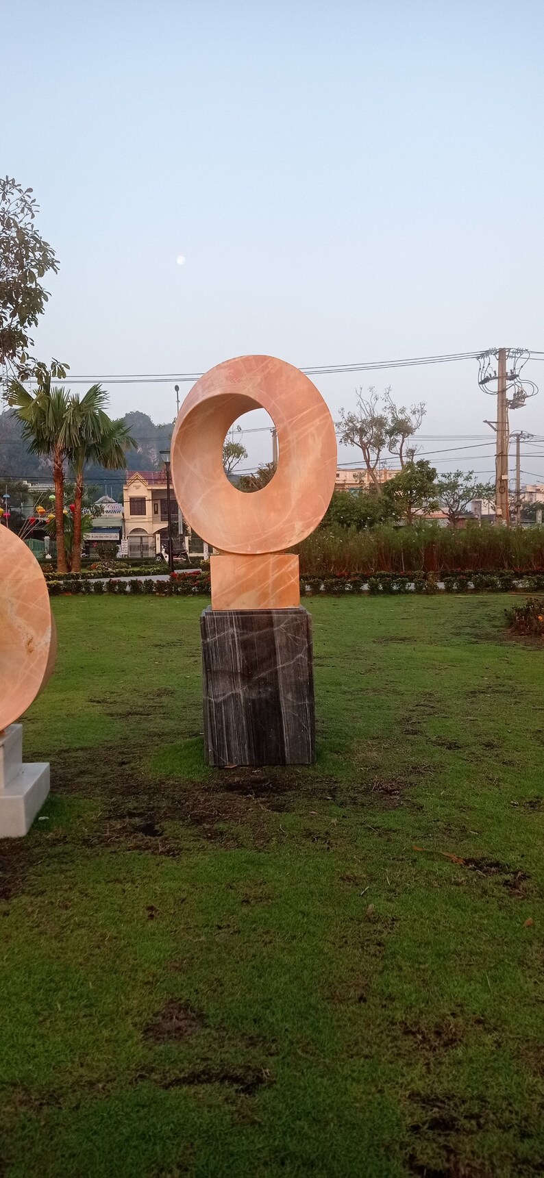 Op de afbeelding: Een modern beeldhouwwerk van roze en zwart marmer. Het beeldhouwwerk heeft de vorm van een ring met een gat in het midden. Het beeldhouwwerk staat op een vierkante basis.