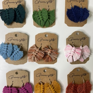 May include: A selection of macrame earrings in shades of teal, green, navy, light blue, brown, pink, purple, yellow, and rust. Each pair is presented on a brown card with the "Greencrafts" logo.