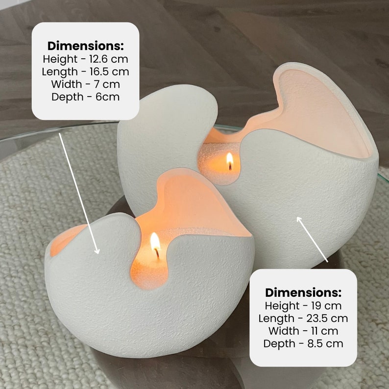 Op de afbeelding: Drie witte, getextureerde, eivormige kaarsen met een uniek ontwerp. Elke kaars heeft een uitsparing die een warme, oranje gloed van de brandende lont onthult. De grotere kaars is 19 cm hoog, 23,5 cm lang, 11 cm breed en 8,5 cm diep.