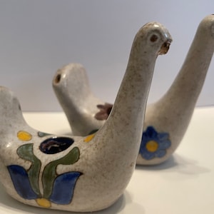 May include: Two ceramic bird salt and pepper shakers with a white base and colorful floral designs. The birds have long necks and are facing opposite directions.