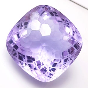 May include: A faceted amethyst gemstone with a cushion cut. The gemstone is a light purple color and has a high polish.