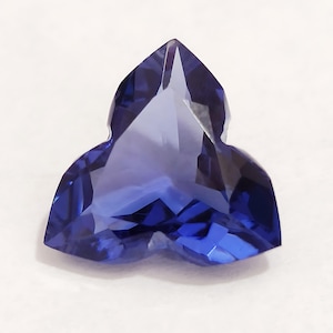 May include: A deep blue, faceted gemstone cut in a triangular shape with three points.