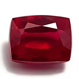 May include: A deep red gemstone with a cushion cut. The gemstone is faceted and has a high polish.