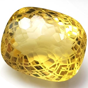 May include: A large, faceted, yellow gemstone with a complex, geometric cut. The stone is translucent and has a warm, golden hue.