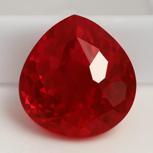 May include: A deep red, faceted, teardrop-shaped gemstone.
