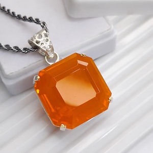 May include: A square, orange gemstone pendant with a silver chain. The gemstone is faceted and set in a silver bezel. The chain is a twisted rope style. The pendant is a striking piece of jewelry.
