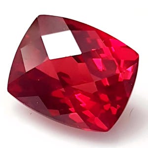 May include: A deep red gemstone with a cushion cut. The gemstone is faceted and has a high polish.