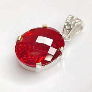 May include: A silver pendant featuring a large, oval-shaped, red gemstone set in a silver and gold setting. The pendant has a silver bail with a decorative design.