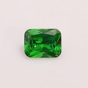 May include: A vibrant green emerald cut gemstone with a faceted finish.