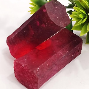 May include: Two large, faceted, red ruby crystals. The crystals are cut into a rectangular shape with rounded edges. The crystals are translucent and have a deep red colour.