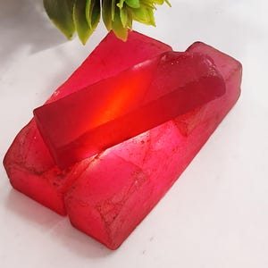 Könnte beinhalten: Eine Gruppe roter, facettierter, roher Edelsteine. Die Edelsteine sind übereinander gestapelt, wobei der oberste Edelstein der größte und auffälligste ist. Die Edelsteine sind durchscheinend und haben einen leichten Schimmer.