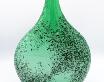 May include: A green glass vase with a unique design of black lines throughout the surface.