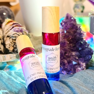 May include: Two small glass bottles with wooden caps and blue and red liquid inside. The bottles are labeled "zenith wellness LLC" and "Retrograde Remedy". The text on the labels reads "Blend Infused Reiki Energy".