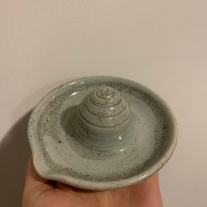 Puede incluir: Un exprimidor de cítricos de cerámica gris claro con un acabado moteado. El exprimidor tiene un exprimidor cónico y una base ancha con un pico.