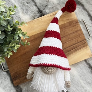 May include: A crocheted gnome with a white beard and a red and white striped hat with a white pom-pom on top.