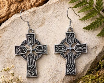 May include: A pair of silver-toned Celtic cross earrings. Each earring features an intricate design with a cross shape, a circular frame, and decorative knotwork. The earrings hang from a simple hook.