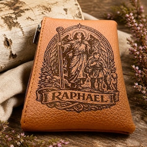 May include: A tan leather wallet with a zip closure. The front displays an engraved image of an angel with a staff, a child, and the name "RAPHAEL". The wallet is set on a wooden surface.